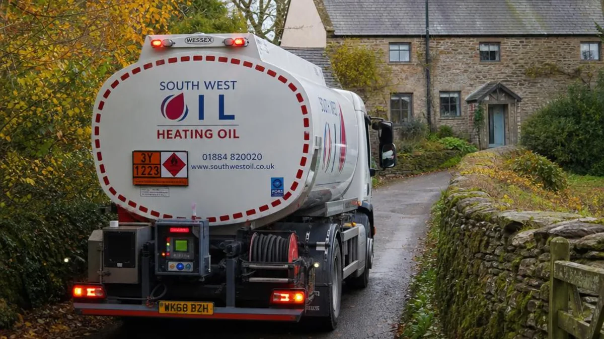 A heating oil delivery tanker navigating a narrow Devon country lane to reach a rural farmhouse